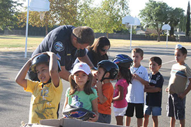 A group of children lined up with police officers putting helmets on them